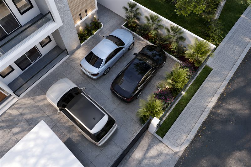 A corner of the parking court from above: three cars on grey pavers, a raised bed of palms and bougainvillea along the boundary wall, and a grass strip at the pavement.