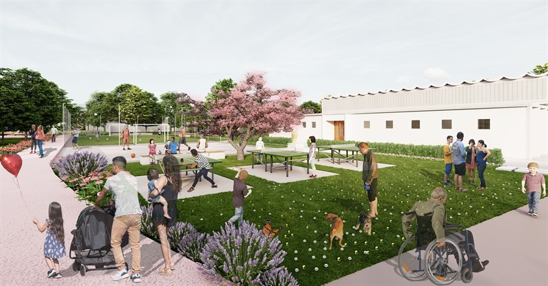 Where Generations Unite: the sports and play edge in use, table tennis tables on the grass under a flowering cherry, a basketball court beyond and the sports hall to the right.