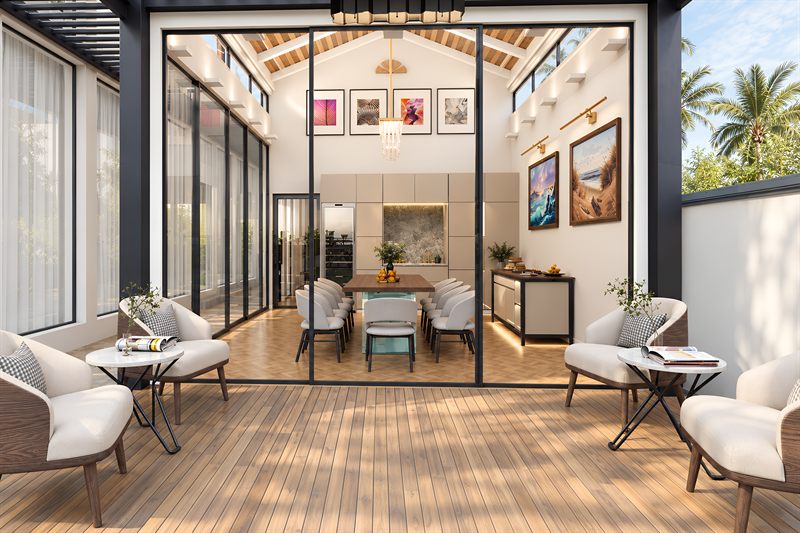 The outhouse dining room seen from the deck: a glazed pavilion under a vaulted ceiling boarded in timber, with a long table inside and armchairs on the timber boards outside.