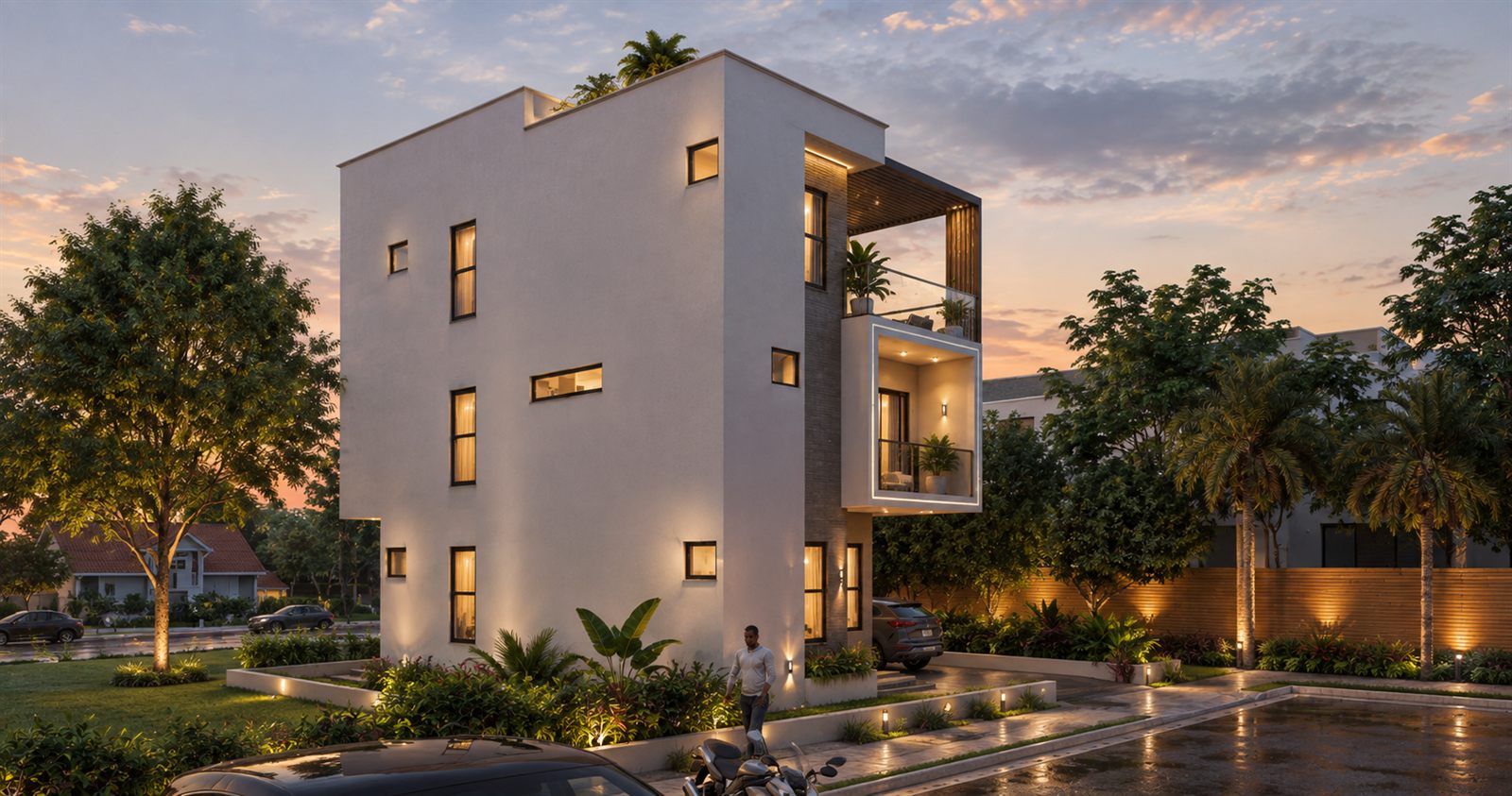 The house at dusk from the side: a plain white rendered wall with small windows on all three floors, the framed balconies and the pergola projecting at the front corner, and lit planting along the drive where a car is parked.