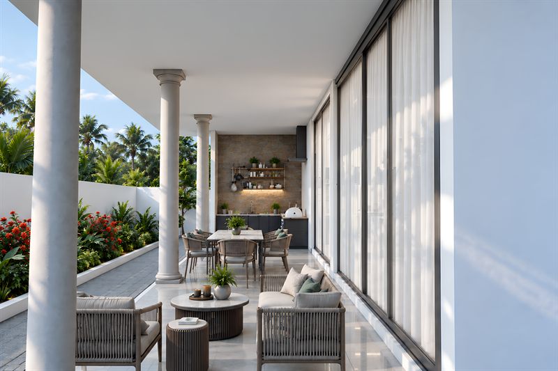 The back porch: round columns down the open left side carrying the roof, full-height sliding glazed doors along the right into the dining area with a stone-clad wall beyond, woven chairs around small round tables on a polished floor, and a low white wall with roses and lawn past it.